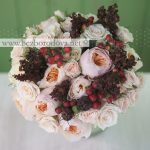 Кремовый свадебный букет из пионовидных роз с красными ягодами и коричневым щавелем.