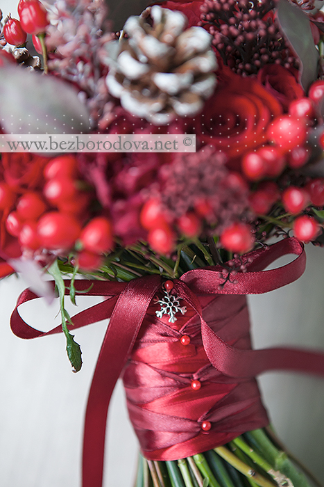 Зимний свадебный букет из красных роз и ранункулюсов с ягодами гиперикума и шишками 