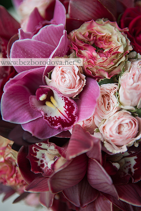 Букет цвета марсала из орхидей цимбидиум, розовых пионовидных роз, красных роз и винного леукадендрона 