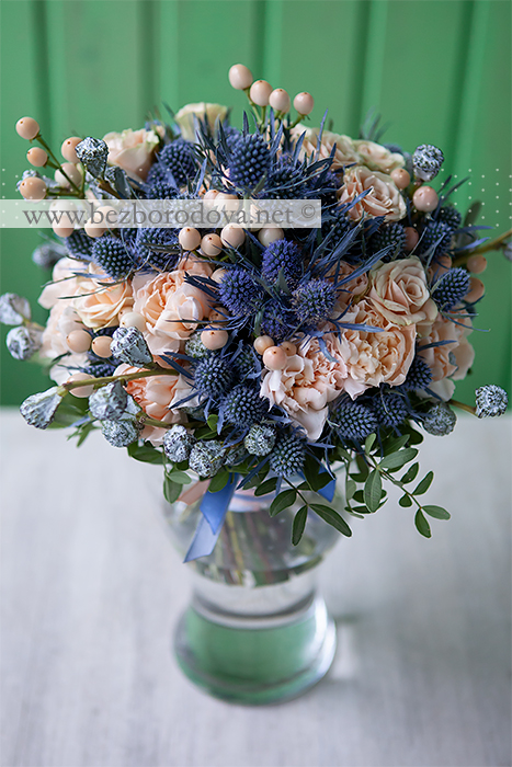 Кремовый свадебный букет из роз и гвоздик с ягодами гиперикума, синими эрингиумами и серыми бутонами эвкалипта